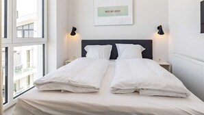 A hotel room with a bed, two bedside tables, a wall-mounted light, and a window.