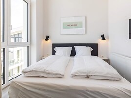 Et hotelværelse med en seng, to sengeborde, en vægmonteret lampe og et vindue.