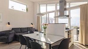 A modern living space with a dining area, a sofa, a kitchen, and large windows.