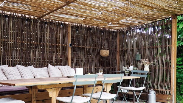 An outdoor dining area with a wooden table and chairs, a woven bamboo fence, and a hanging light fixture. - 5 Person Holiday Home in Bogo By (Bogø By)