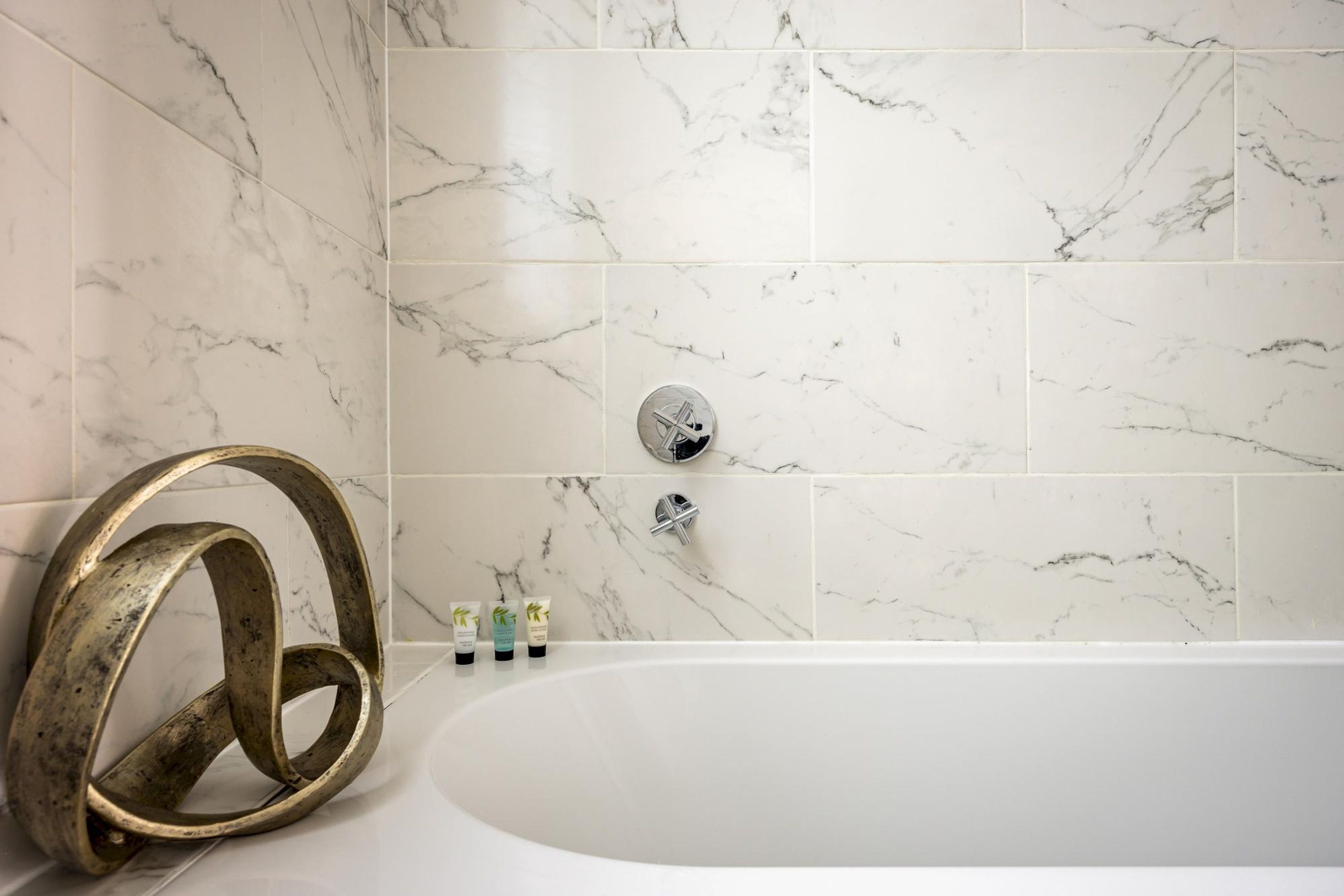 Ein Badezimmer mit einer Wand aus Marmorfliesen, einer Badewanne und einem dekorativen Metallring.