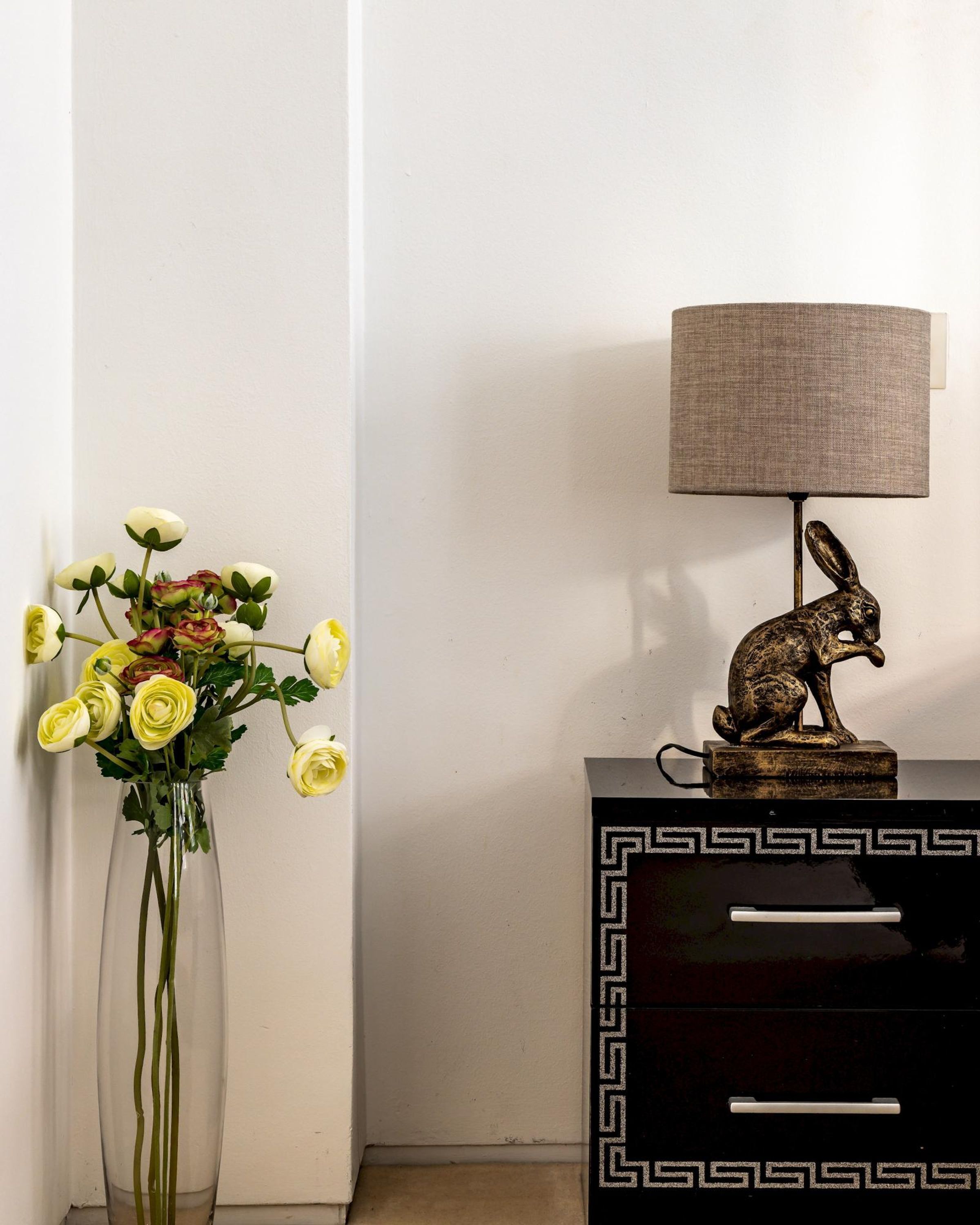 Un jarrón con flores amarillas, una lámpara con una figurita de conejo y un mueble negro con un diseño geométrico.