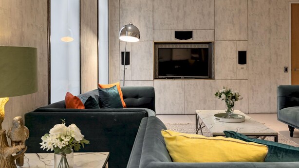 Een moderne woonkamer met een grote flatscreen televisie aan de muur, een bank met meerdere kussens, een bijzettafel met een bloevas en een vloerlamp.