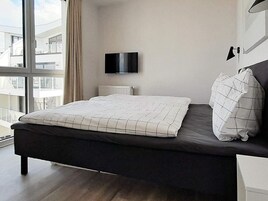 A modern bedroom with a bed, a television, and a window with a view of buildings.