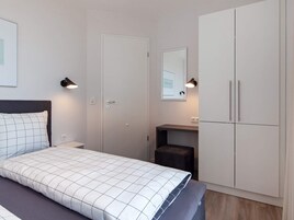 Un dormitorio con cama, mesitas de noche, armario y escritorio con silla.