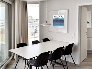 A modern dining area with a white table and black chairs, a pendant light, and a framed poster on the wall. - 5 Star Holiday Home in Wendtorf (Wendtorf)