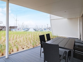 Un patio al aire libre con vistas a un puerto deportivo y una zona arenosa con plantas jóvenes.