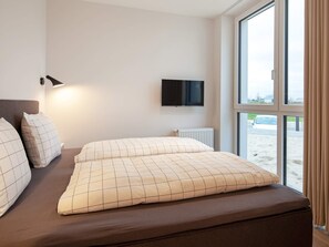 Une chambre d’hôtel avec un lit, un téléviseur fixé au mur et une fenêtre donnant sur la plage.