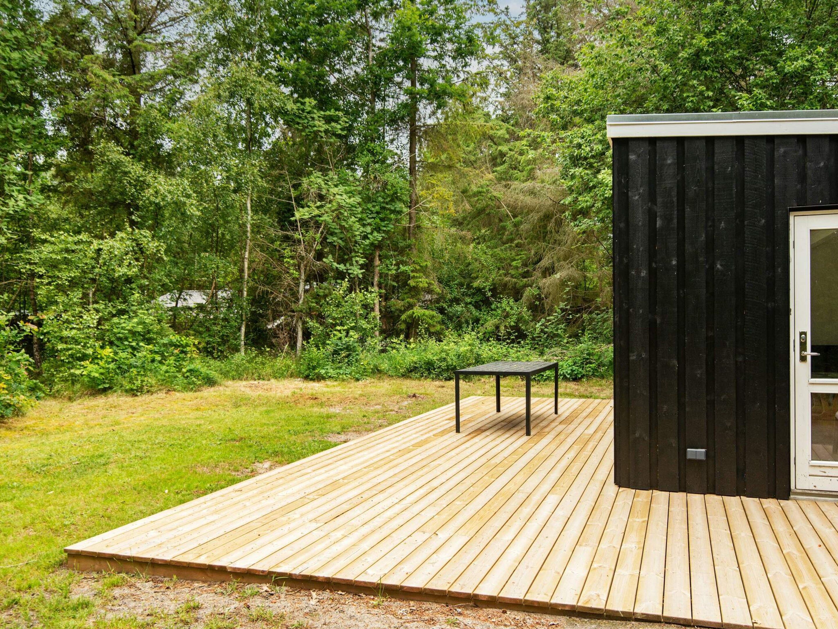 A wooden deck with a table and a small shed in a wooded area.