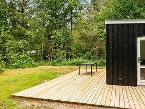 Una terraza de madera con una mesa y un cobertizo pequeño en una zona boscosa.
