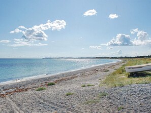 A beach with a boat on the shore, clear sky, and distant land. - 4 Person Holiday Home in Ebeltoft (Ebeltoft)