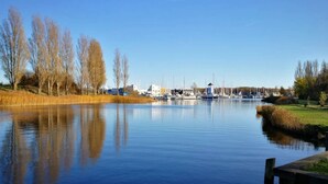 A calm lake with boats, a dock, and buildings in the background. - 4 Person Holiday Home in Ebeltoft (Ebeltoft)