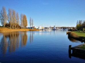 A calm lake with boats, a dock, and buildings in the background. - 4 Person Holiday Home in Ebeltoft (Ebeltoft)