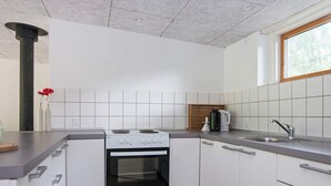 A compact kitchen with white cabinets, a stove, a sink, and a window. - 4 Person Holiday Home in Ebeltoft (Ebeltoft)
