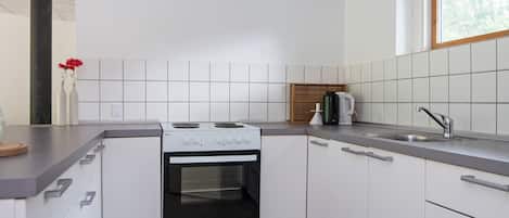 Cocina compacta con gabinetes blancos, estufa, pileta y ventana.
