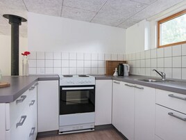 Cocina compacta con gabinetes blancos, estufa, pileta y ventana.
