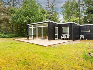A modern, black wooden house with large glass windows, a wooden deck, and two white plastic chairs. - 4 Person Holiday Home in Ebeltoft (Ebeltoft)