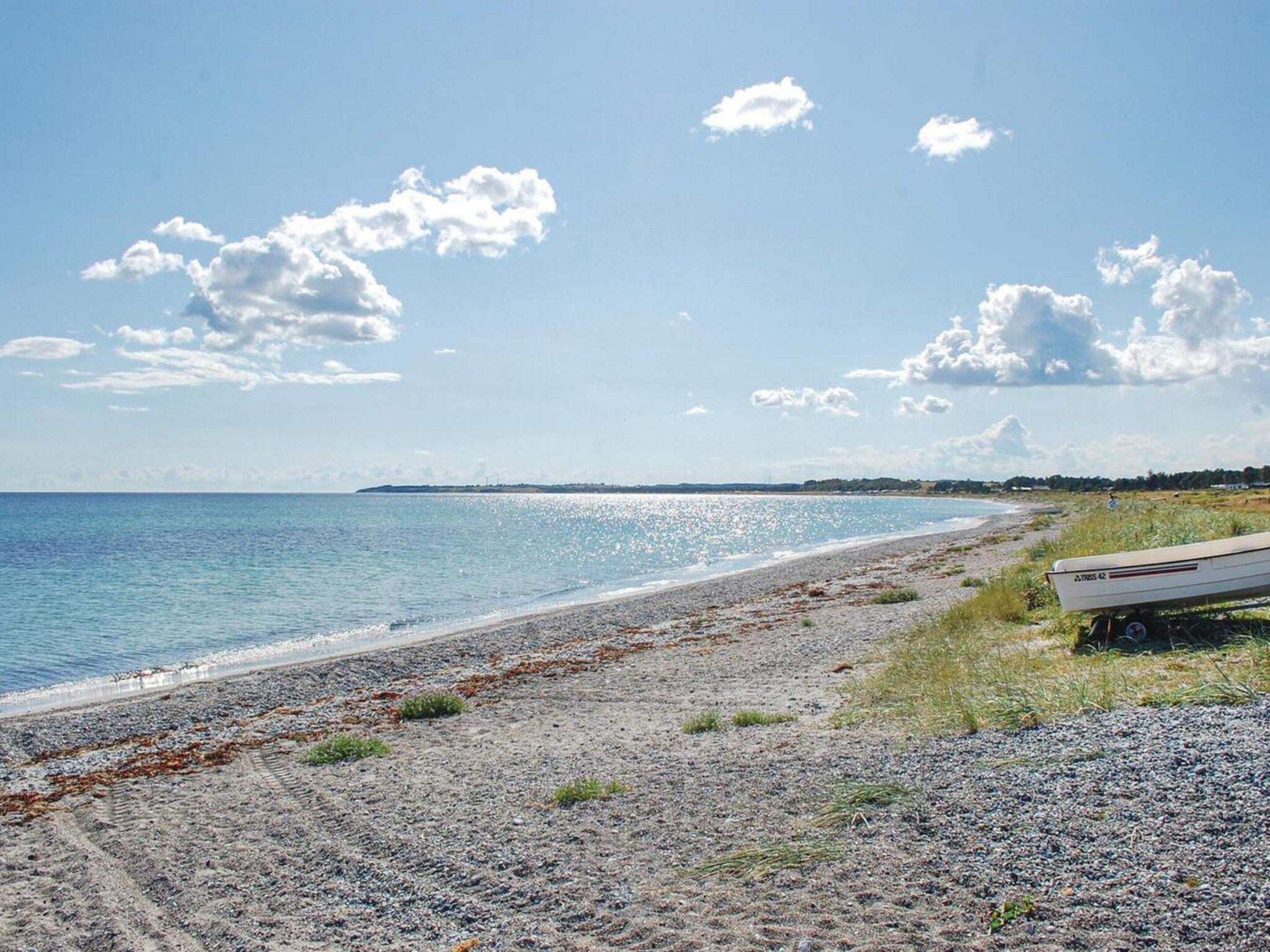 A beach with a boat on the shore, a clear sky, and distant land.