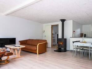 Una sala de estar con sofá, una mesita redonda, televisor, chimenea y un comedor con sillas.