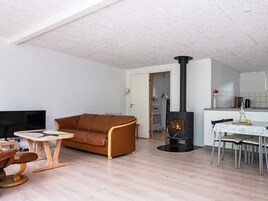 Sala de estar com sofá, mesa redonda pequena, TV, lareira e área de jantar com cadeiras.