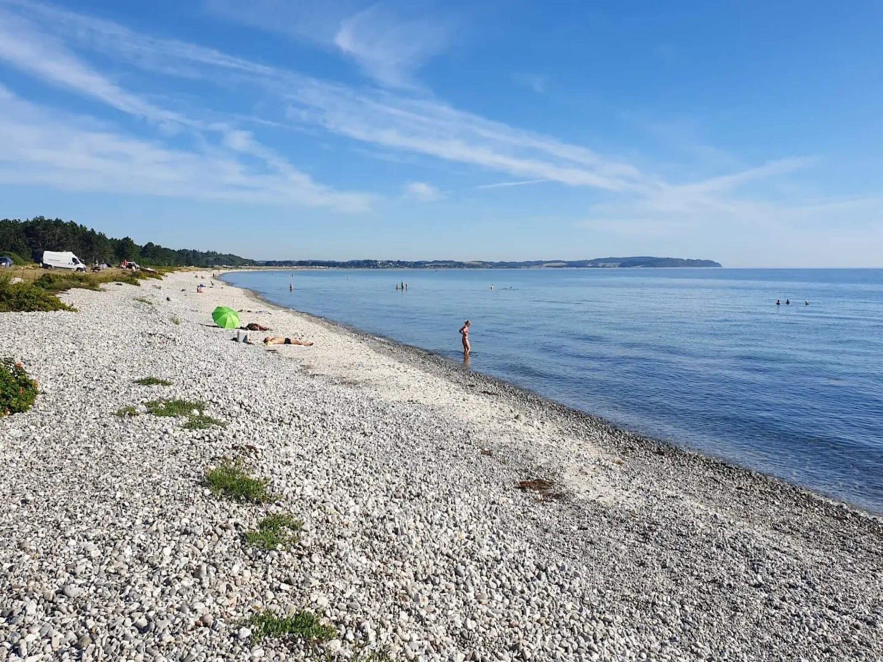A pebbled beach with a clear sky, a few people, and a distant shoreline.
