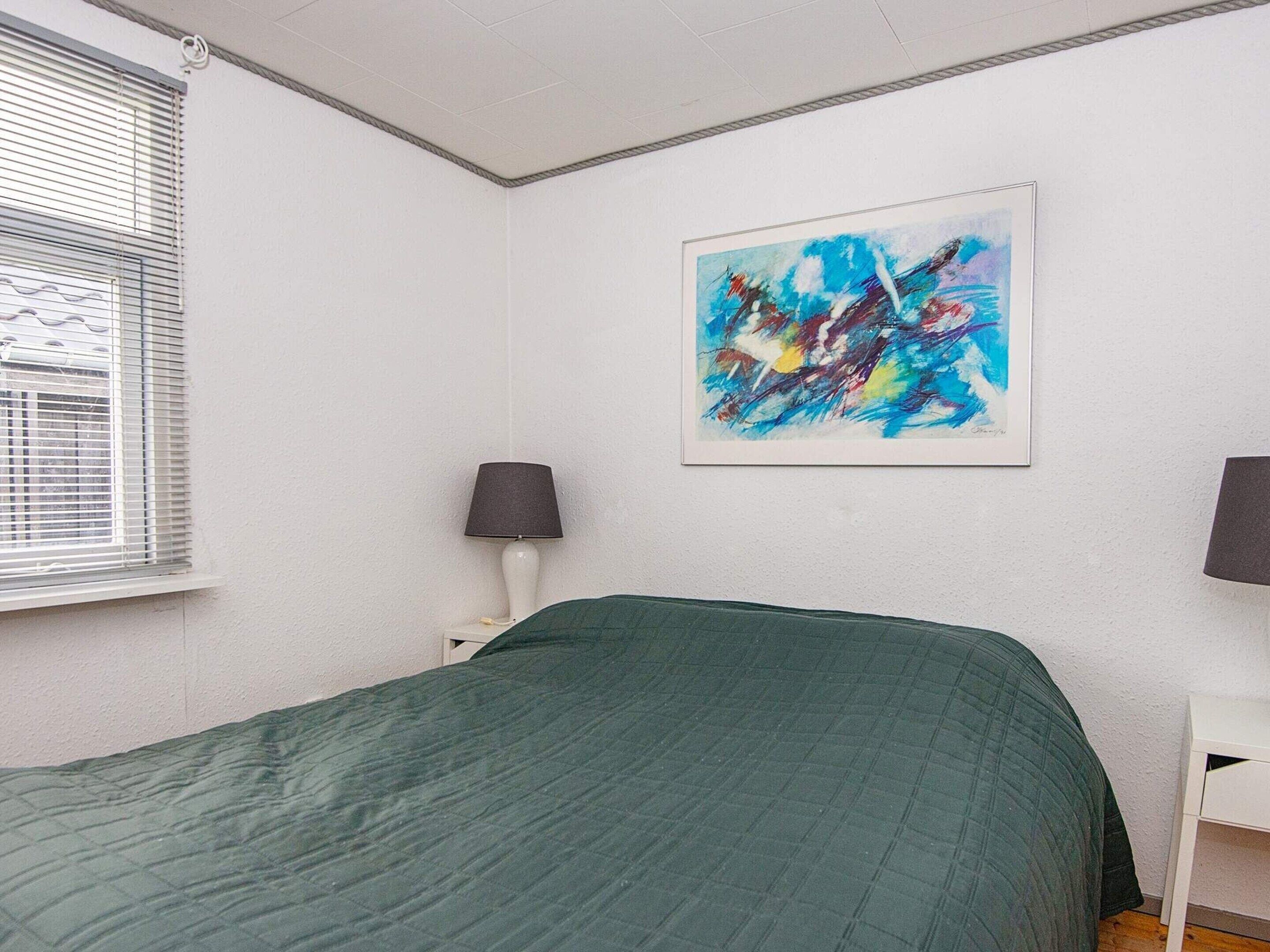 A bedroom with a green bedspread, a white wall, and a colorful abstract painting.