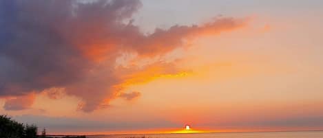 A sunset over a body of water with a grassy foreground and a few people sitting on the shore.