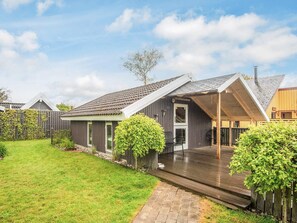 Ett modernt hus med en inglasad veranda, en välskött gräsmatta och ett trästaket.
