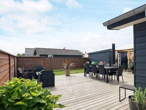 An outdoor patio with a wooden deck, a dining table, and chairs.