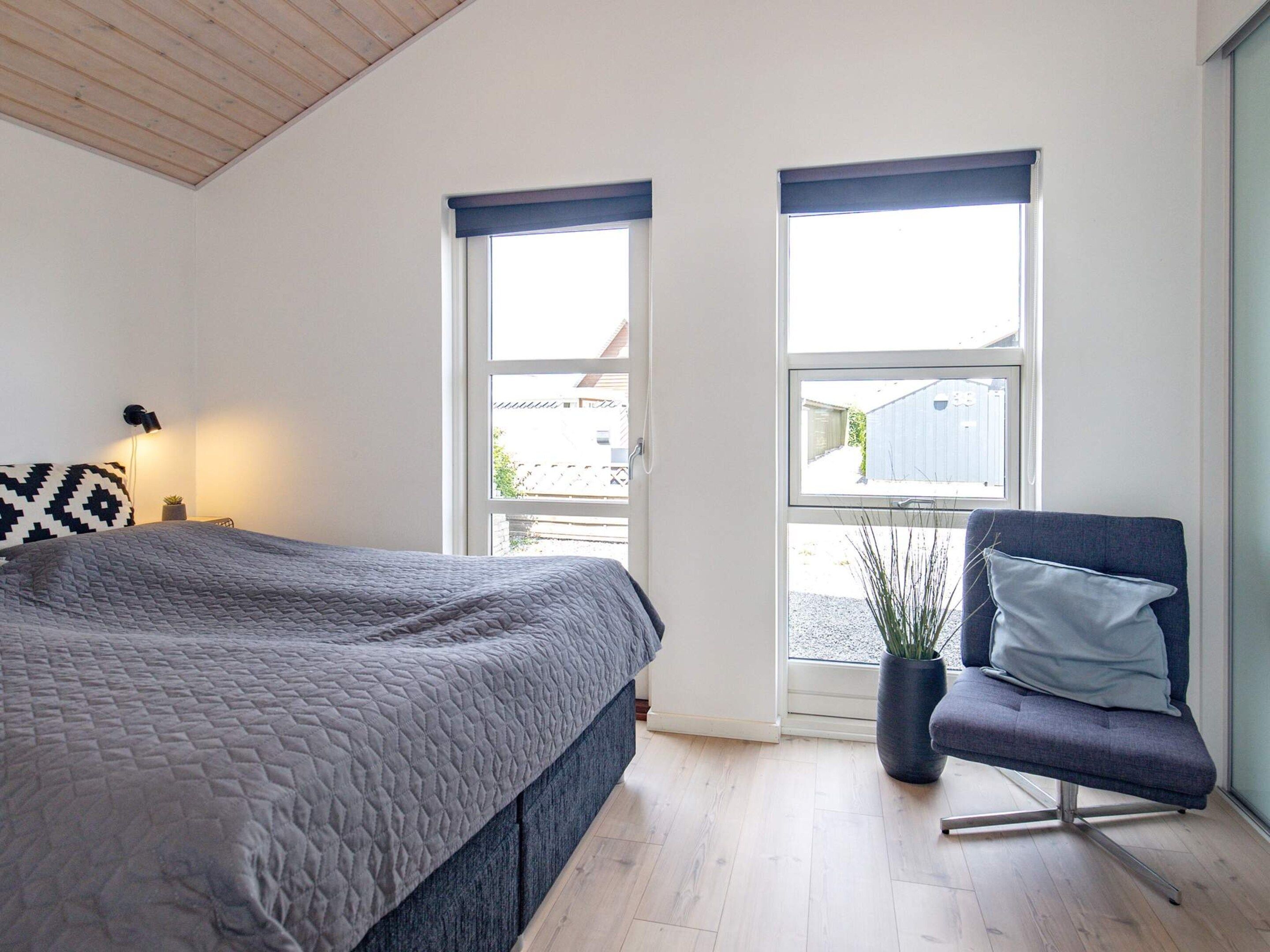 A bedroom with a bed, two windows, a chair, and a lamp.