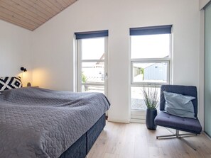 A bedroom with a bed, two windows, a chair, and a lamp.