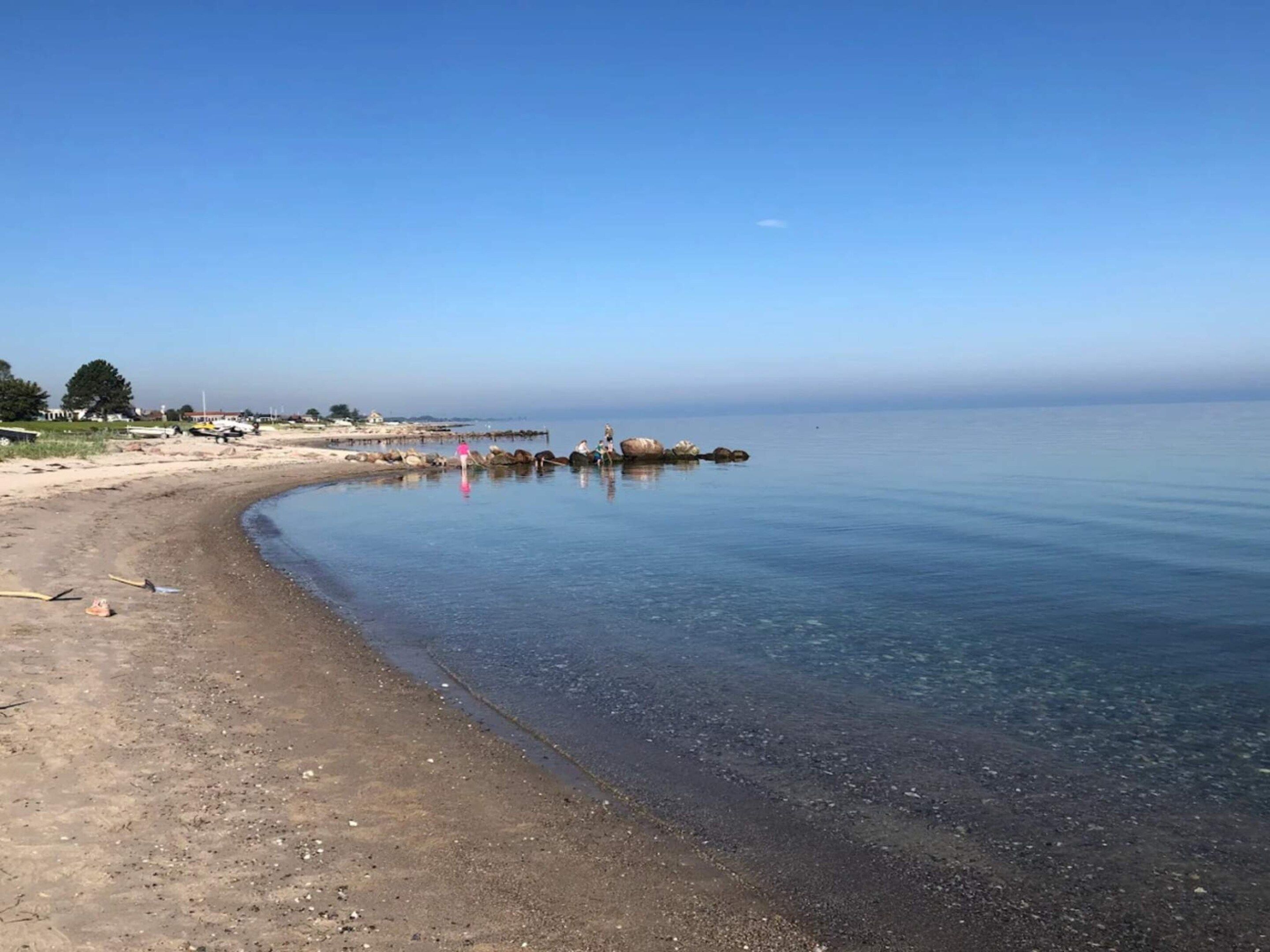 A beach with clear water, a sandy shore, and a distant pier.