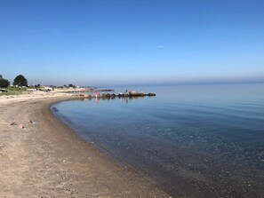 A beach with clear water, a sandy shore, and a distant pier.