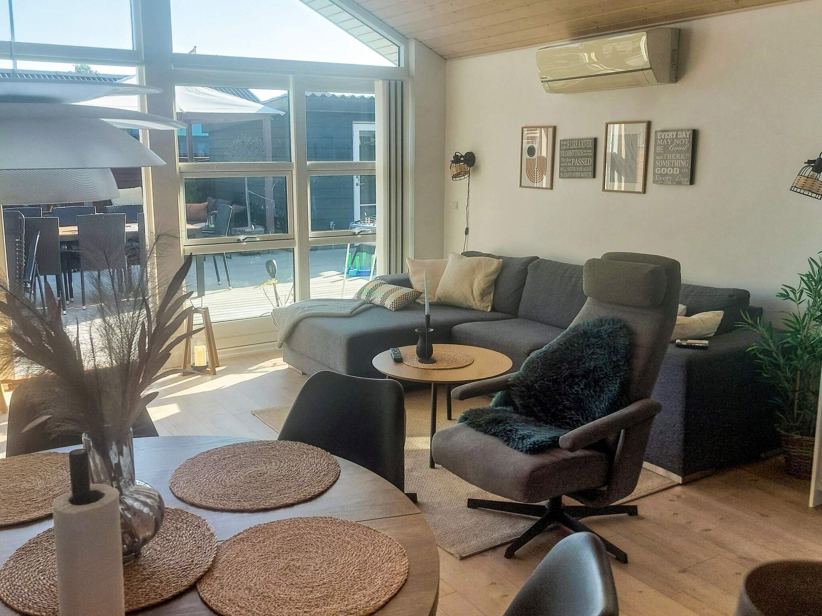A modern living room with a sofa, armchair, and coffee table. There are framed pictures on the wall and a large window providing natural light.