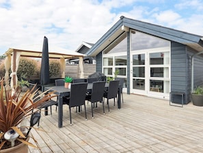 A deck with a dining table and chairs, a grill, and a pergola with curtains. - 4 Star Holiday Home in Otterup (Otterup)