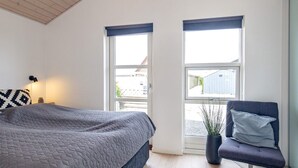 Ein Schlafzimmer mit einem Bett, einem Sessel, einem Fenster und einer Pflanze.