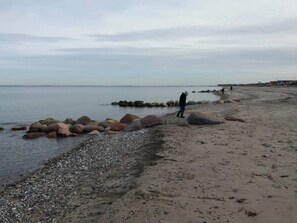 A pebbly beach with large rocks and a person walking. - 4 Star Holiday Home in Otterup (Otterup)