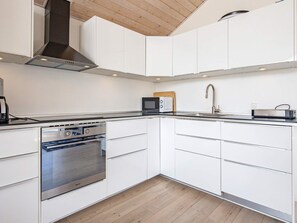 A modern kitchen with white cabinets, a stainless steel oven, a microwave, and a sink. - 4 Star Holiday Home in Otterup (Otterup)