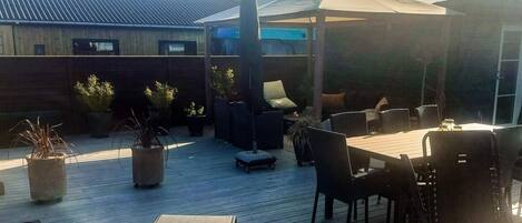 En udendørs terrasse med et bord og stole, plantekasser og en overdækket siddeplads.