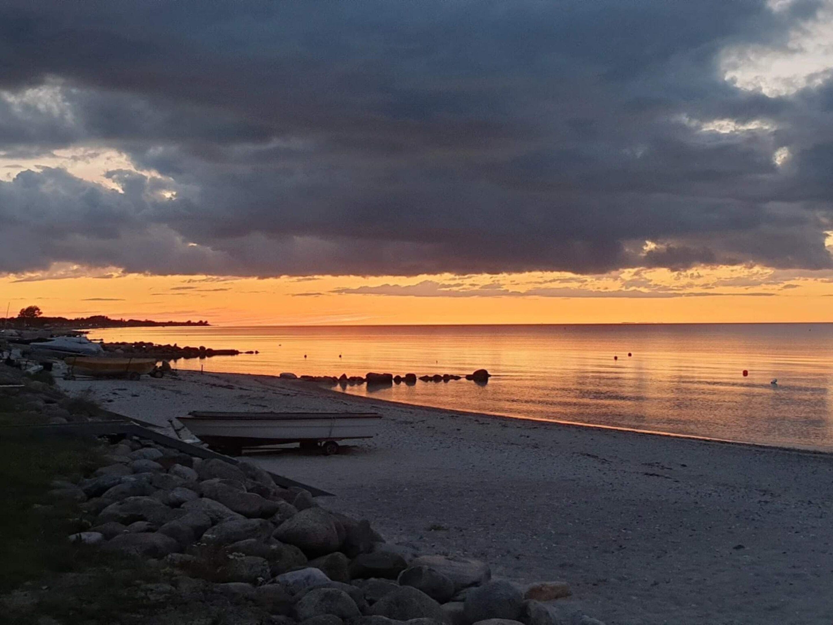 A beach with a rocky shoreline, a calm sea, and a sunset.