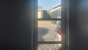 Blick durch eine Tür auf einen klaren Himmel, ein Gebäude und einen geparkten Wagen.