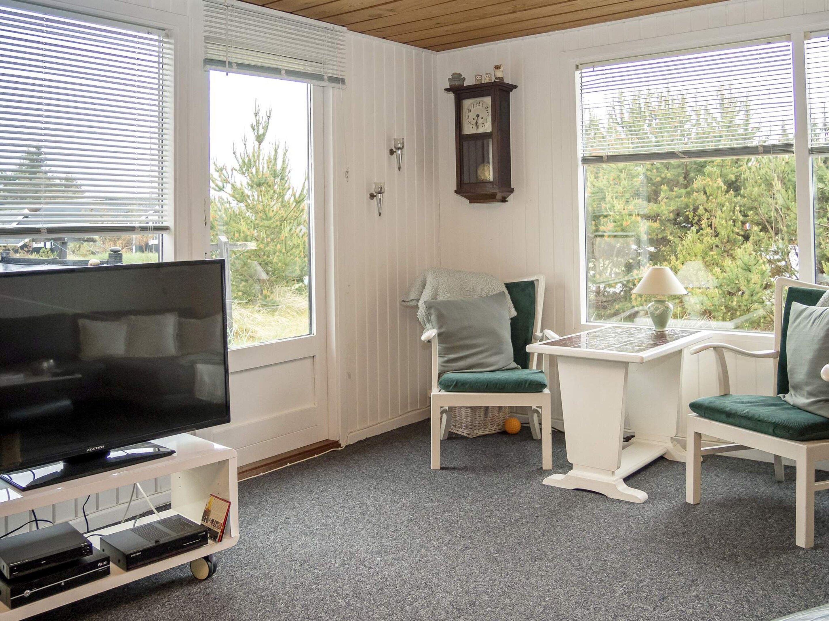 A cozy room with a television on a stand, a clock on the wall, and a window with blinds.