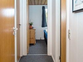En smal gang fører til et rum med en seng, et skrivebord og et vindue med gardiner.
