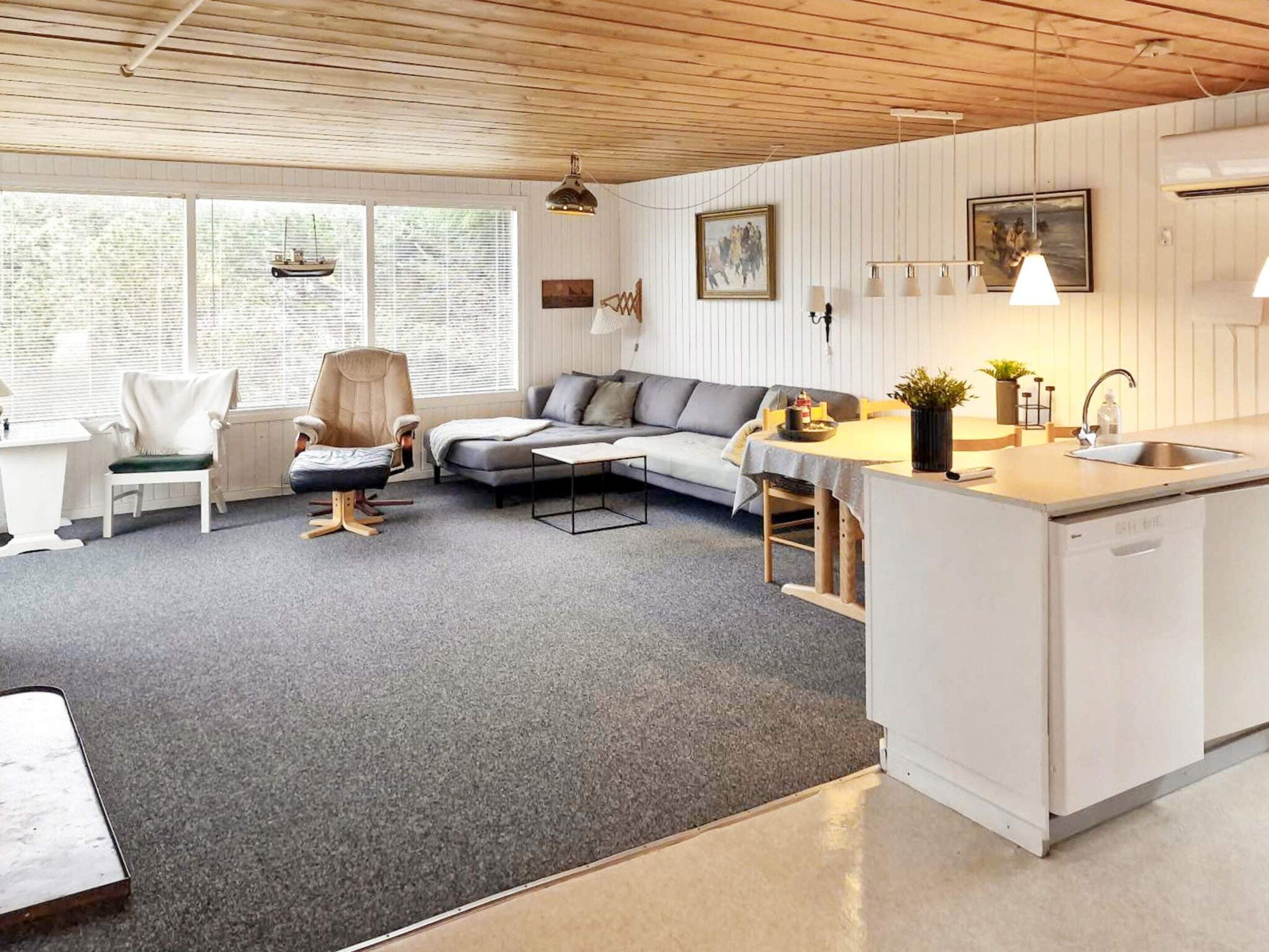 Un salón moderno con un sofá gris, una zona de comedor blanca y una cocina con un fregadero.