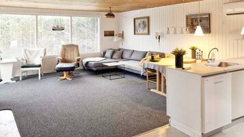 Un salón moderno con un sofá gris, una zona de comedor blanca y una cocina con un fregadero.