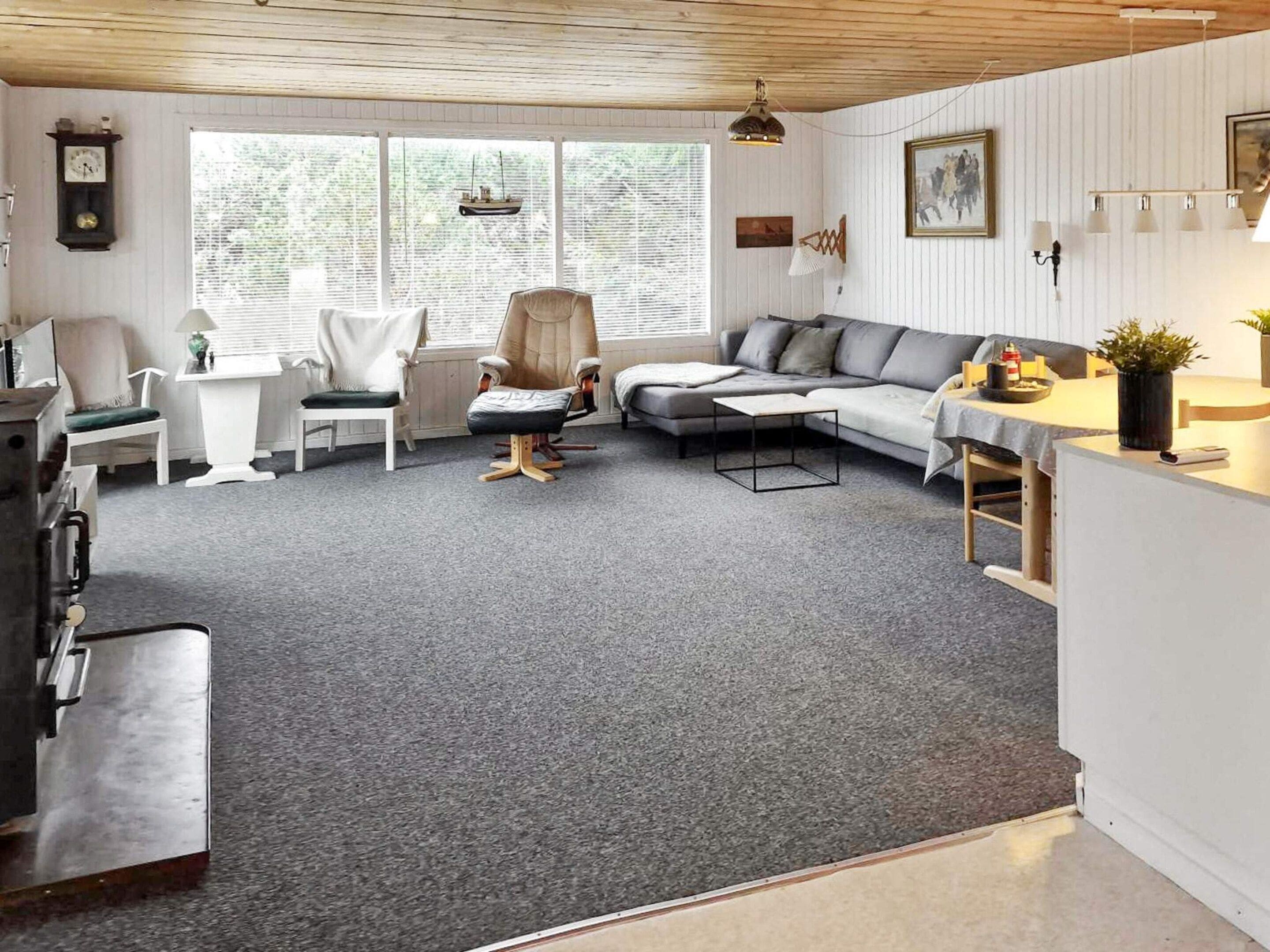 Una sala de estar acogedora con alfombra gris, un sofá, una silla y una mesa de comedor.