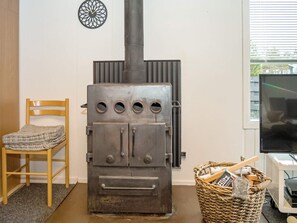 Ett rum med en vedeldad kamin, en stol, en tv och en korg av rotting som innehåller diverse föremål.
