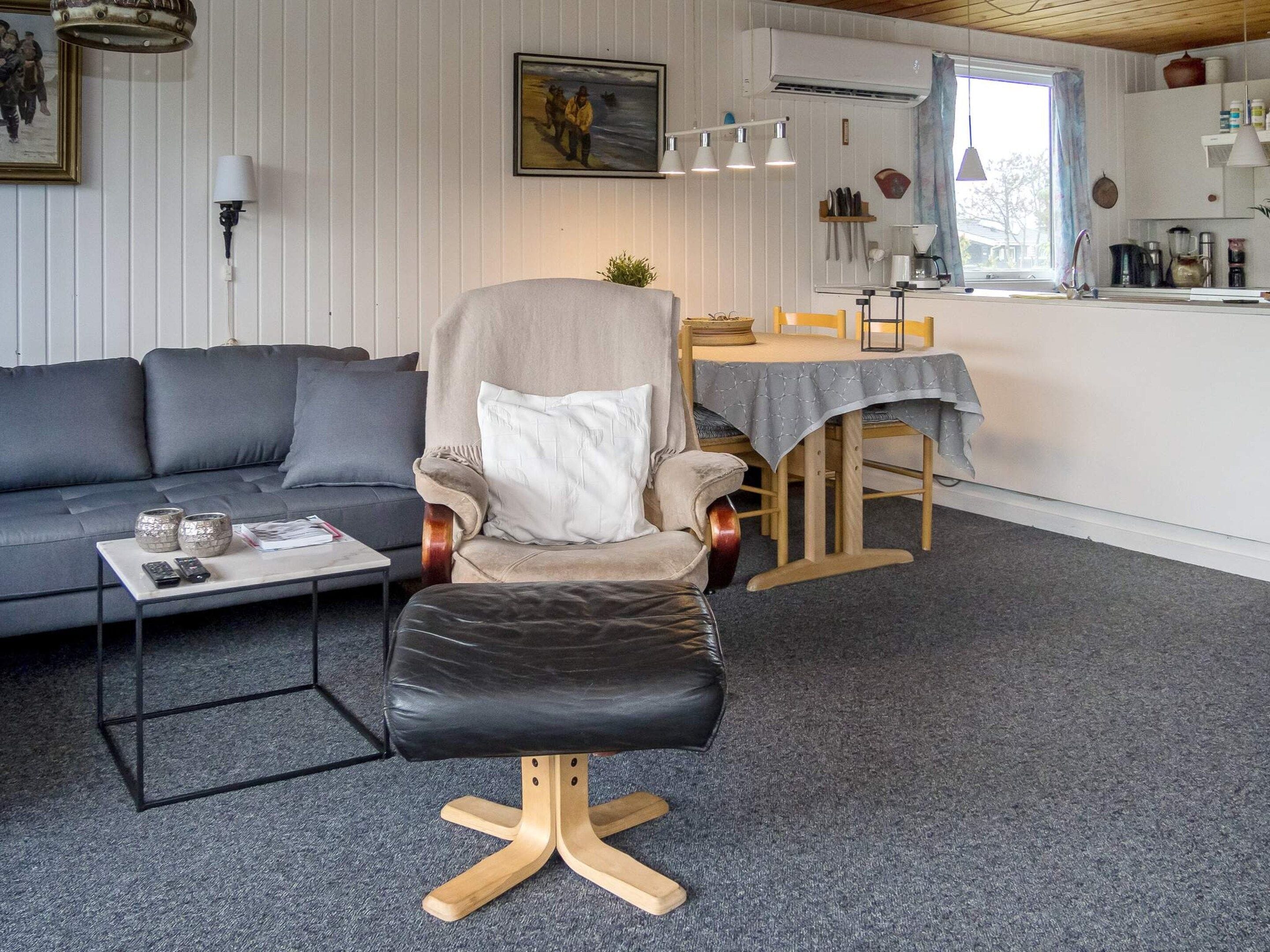 Una sala moderna con un sofá, un sillón de cuero, una mesa de comedor con sillas y una cocina al fondo.