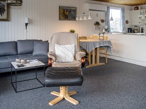 A modern living room with a sofa, a leather chair, a dining table with chairs, and a kitchen area in the background. - 6 Person Holiday Home in Thisted (Thisted)