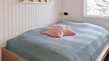 A bedroom with a bed, a window, and a wall-mounted shelf with framed pictures.